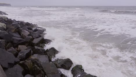 Vista-En-Cámara-Lenta-Del-Mar-Chocando-Contra-Las-Rocas-En-Un-Día-Aburrido,-Whitby,-Yorkshire-Del-Norte,-Inglaterra,-Reino-Unido