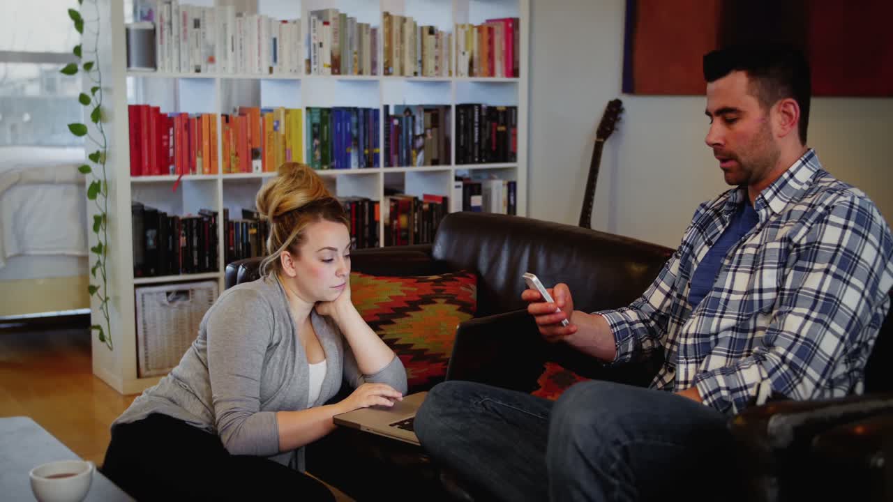 mujer usando computadora portátil mientras el hombre usa teléfono móvil en la sala de estar