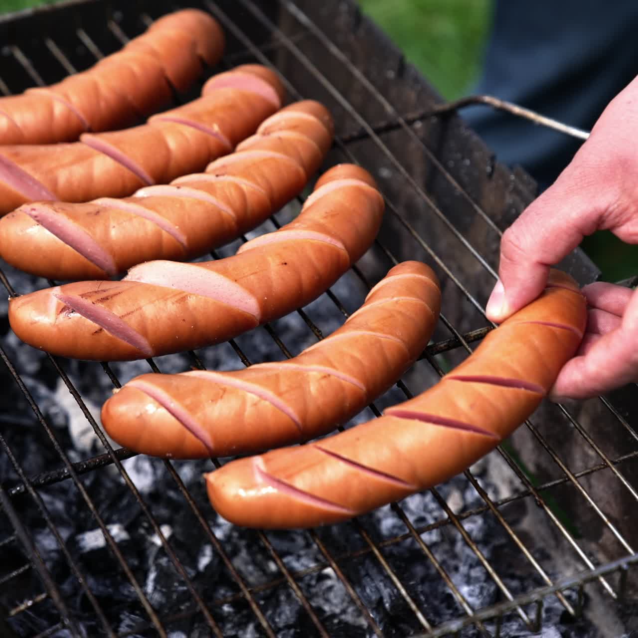 Preparation for grilling sausages. Sausages with incisions on the grill. Process of preparing tasty hot dogs. Barbeque outdoors. Time for picnic
