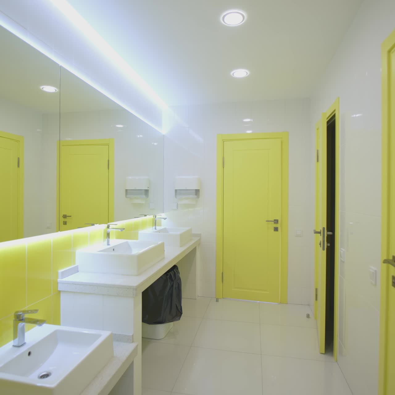 Washroom in white and yellow colors. Contemporary water closet with clean sinks in hospital. Interior of sterile lavatory