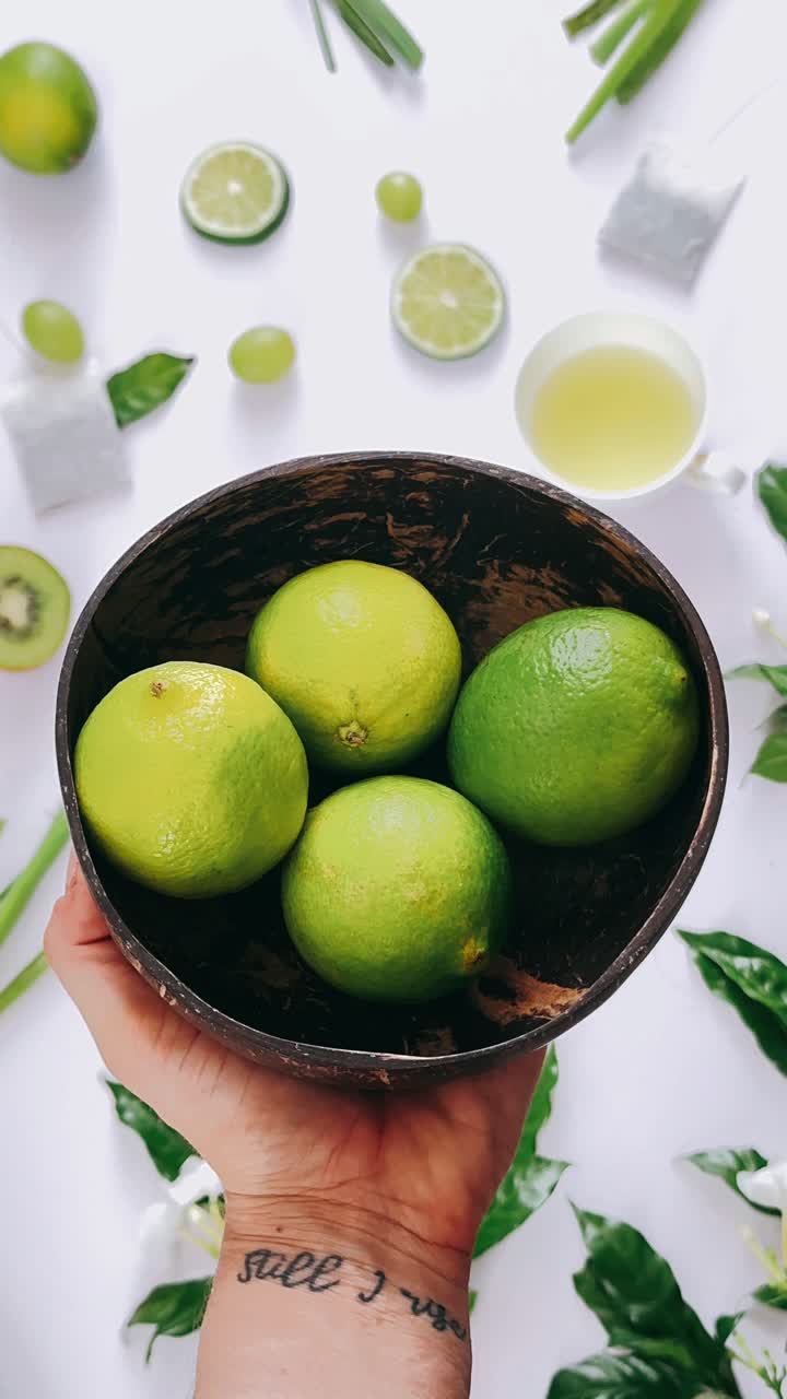 Hand Holding Coconut Bowl with Limes and Fresh Produce