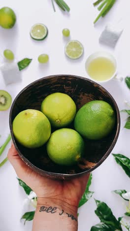 hand holding coconut bowl with limes and fresh produce