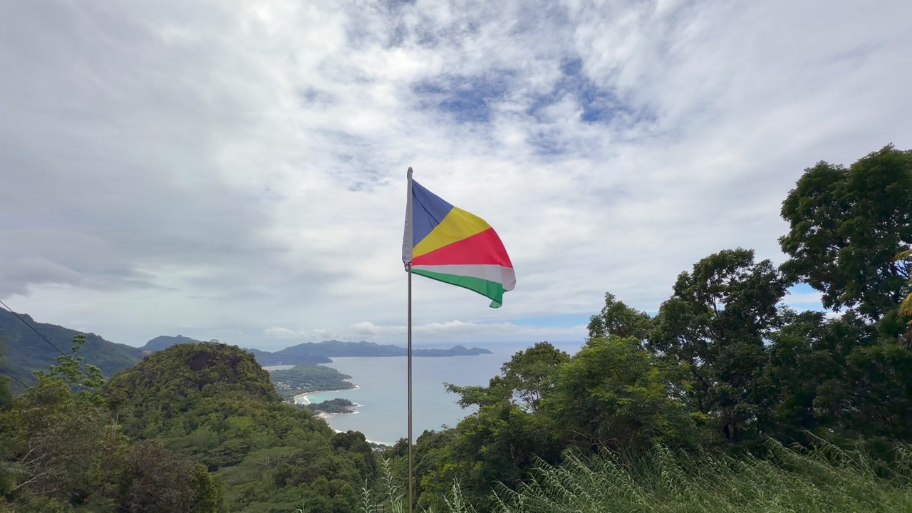 Seychelles flag floating above hill, from the national park, panoramic view of the western coast, Mahe, Seychelles 60fps 001.