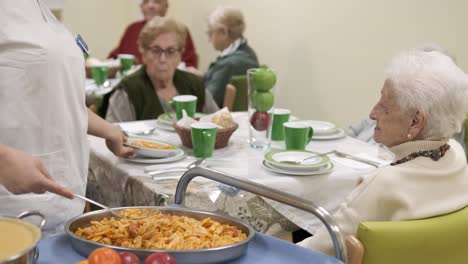 crop worker serving pasta in plate for elderly people