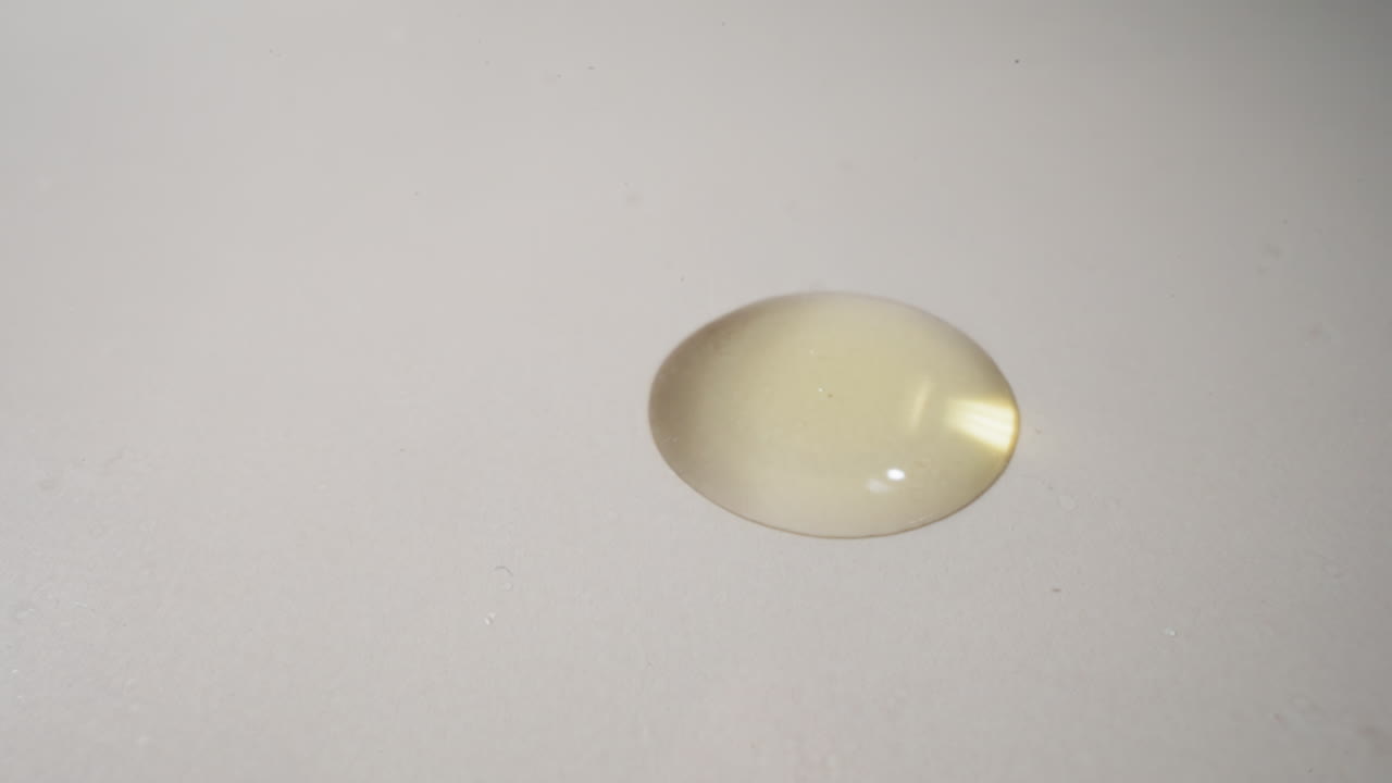 una gota dorada de aceite fresco de jojoba cae extendiéndose por la superficie