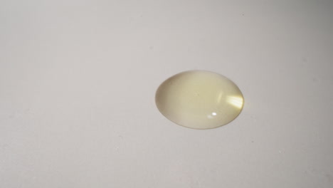 golden drop of fresh jojoba oil falls spreading on surface