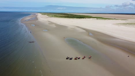 Drone-shot-people-horse-riding-on-sand-beach-in-beautiful-summer-sun