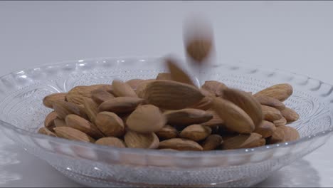 fotografía estática de cerca de almendras sin cáscara cayendo en un plato vacío en la mesa