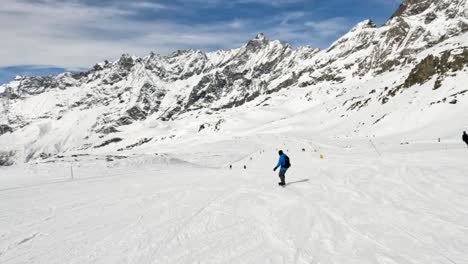 Chase-view-of-snowboarder-descend-on-snowy-slope-with-rocky-mountain-peak-in-Cervinia