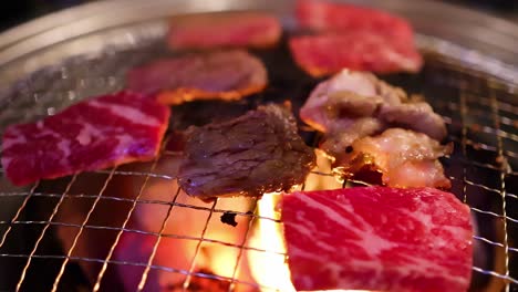 close-up view of marbled meat slices sizzling over a hot charcoal grill with visible flames.