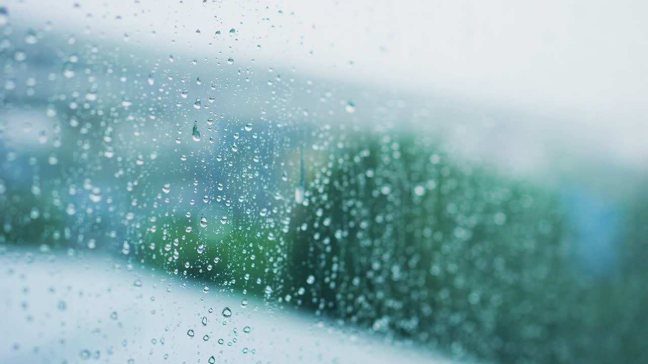 비가 오는 계절을 위한 녹색 공원 배경으로 창문 유리 위에 물이 떨어지는 느린 동작 장면
