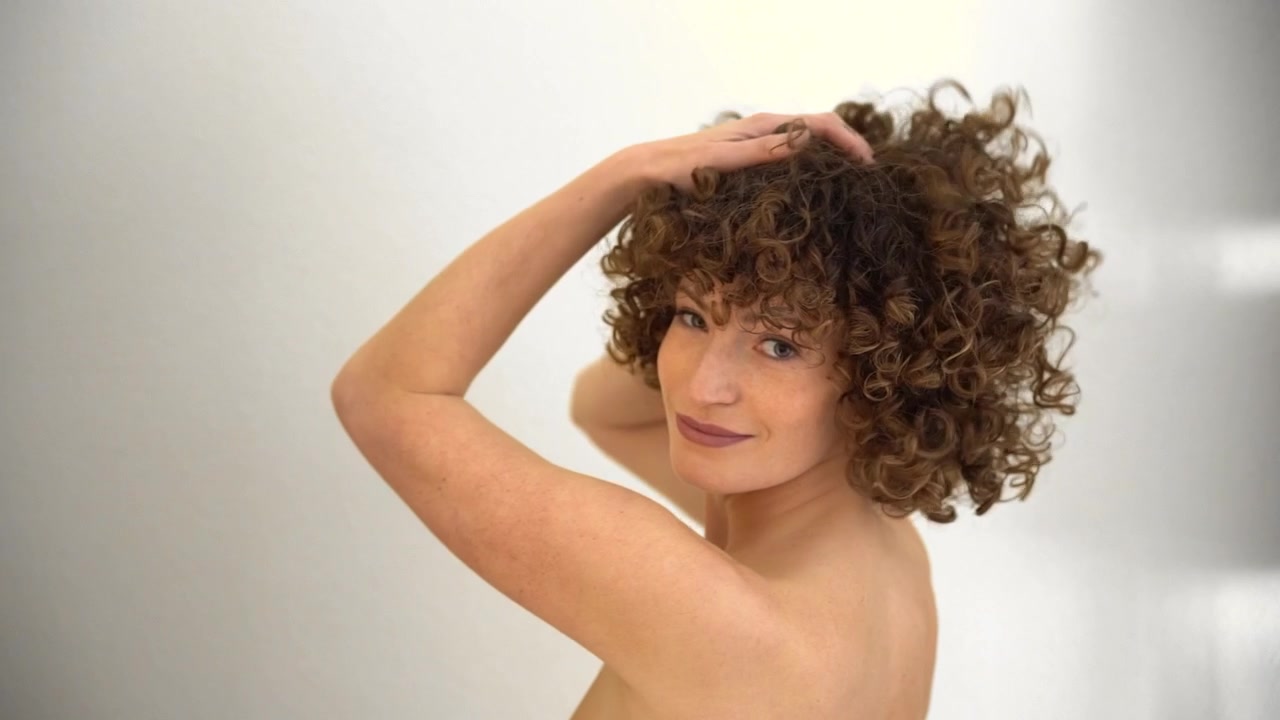 Vista traseira de uma jovem atraente brincando com as mãos em seu cabelo afro encaracolado.