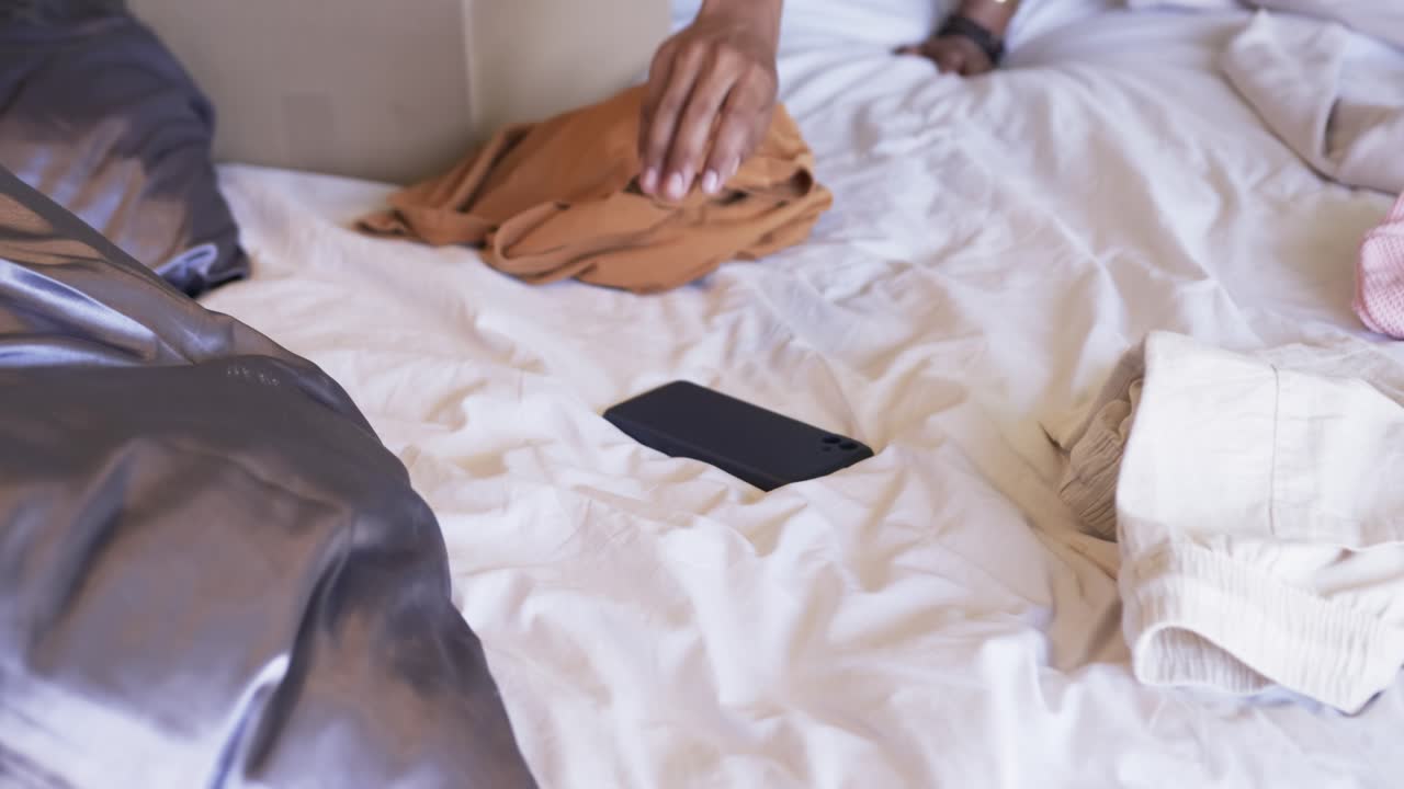 Man seeing face-up black phone on white bed, reaching across, touching sliding grasping retrieving