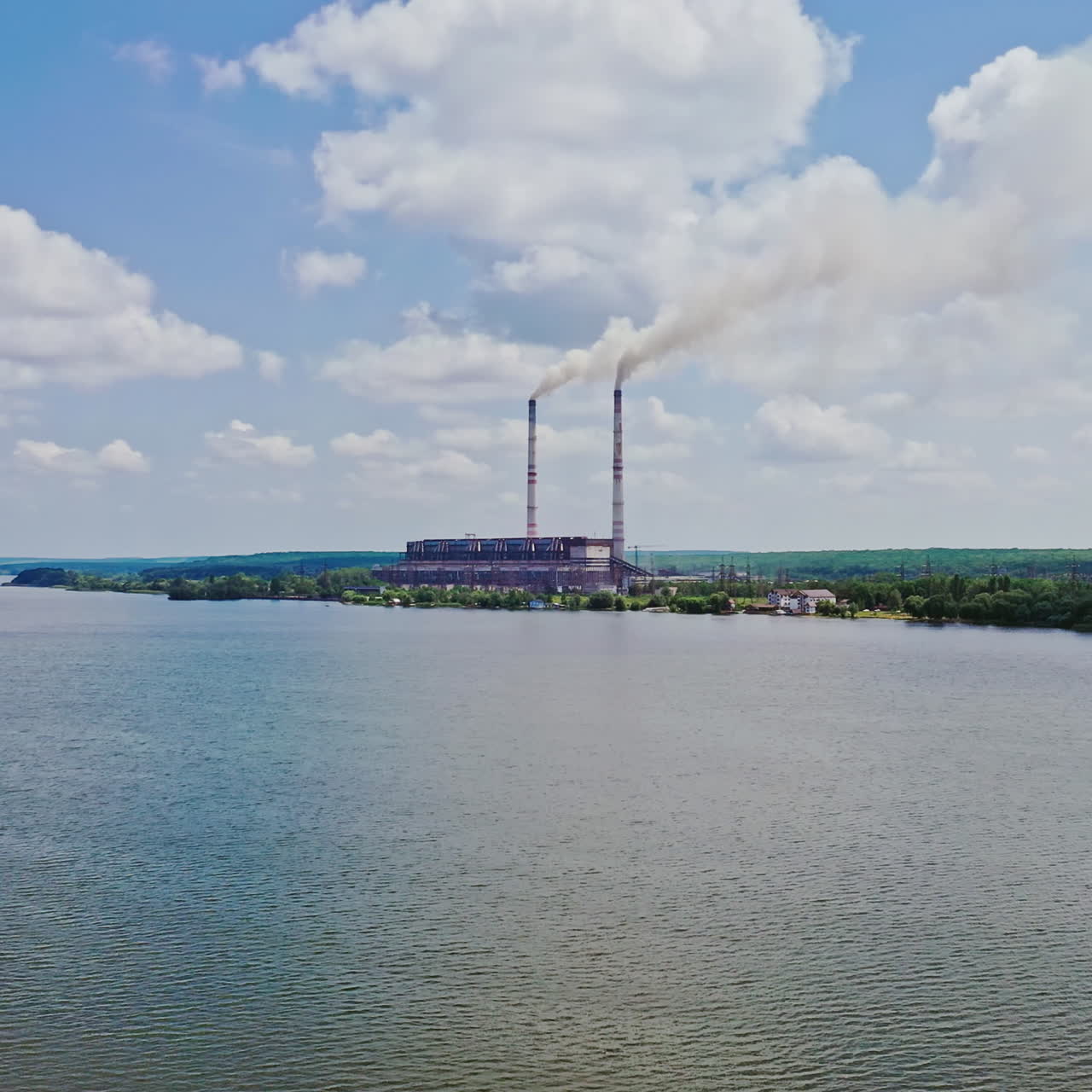 River view from above and two pipes of factory plant. Smoke from the pipes of power plant station at the bank of a river in summer. Aerial view.