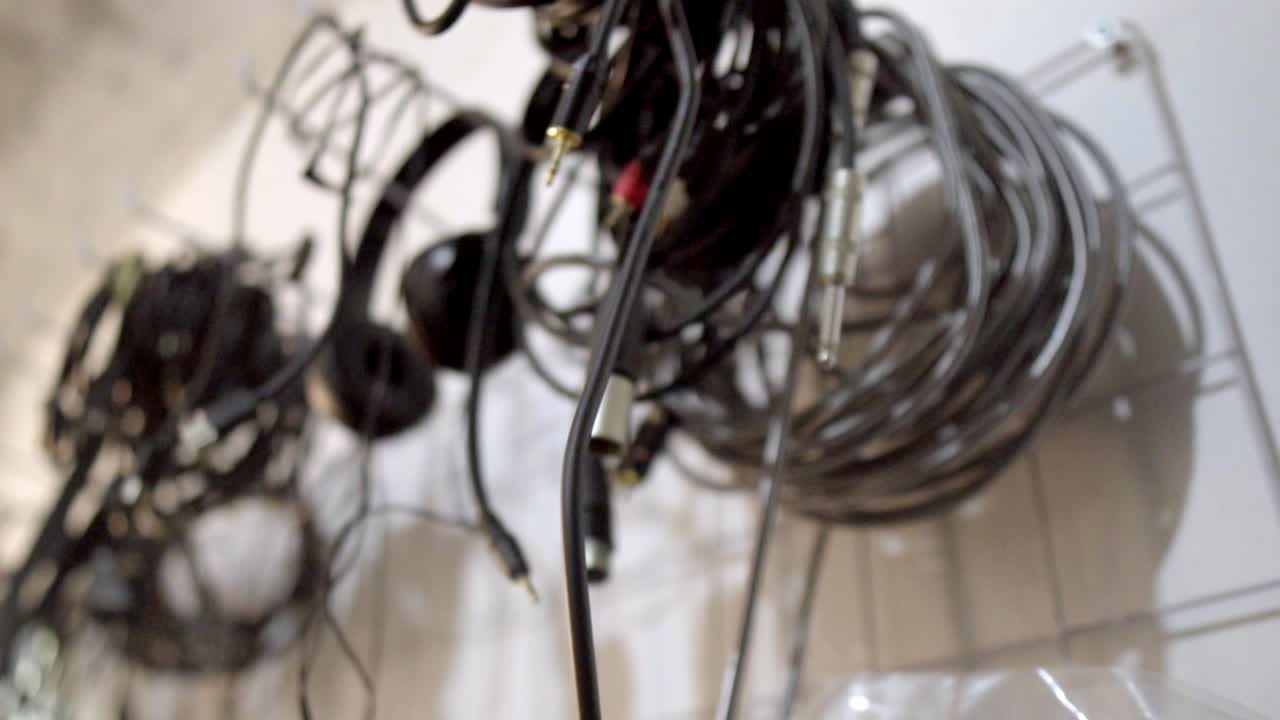 Close up of various tangled audio cables, jack connectors, and headphones hanging in a music recording studio