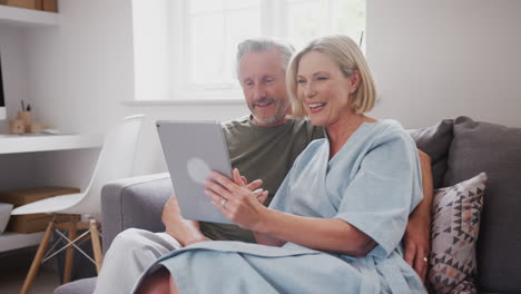 Älteres-Paar-Sitzt-Zu-Hause-Auf-Dem-Sofa-Und-Führt-Gemeinsam-Videoanrufe-Mit-Einem-Digitalen-Tablet-Durch