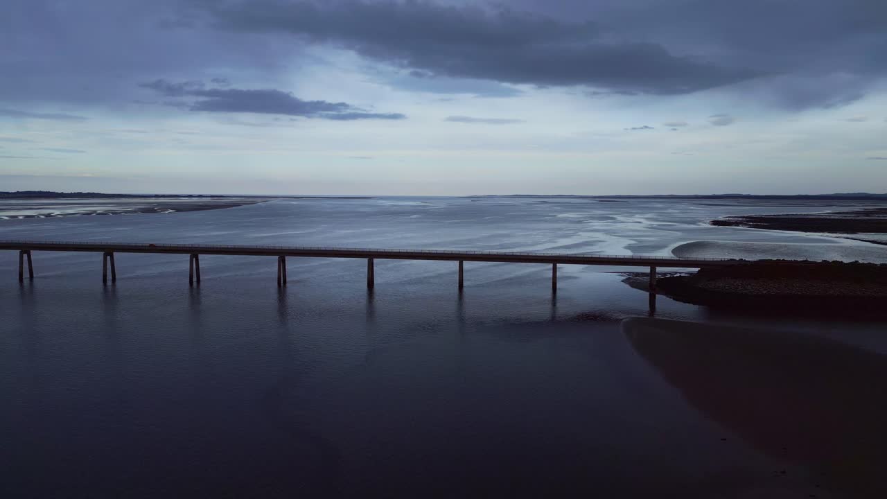 스코틀랜드의 거대한 바다를 가로지르는 인상적인 다리로 향하는 비행, 매혹적인 해가 지는 색채로, 다리는 공학과 자연의 아름다움의 증거로 서 있습니다.
