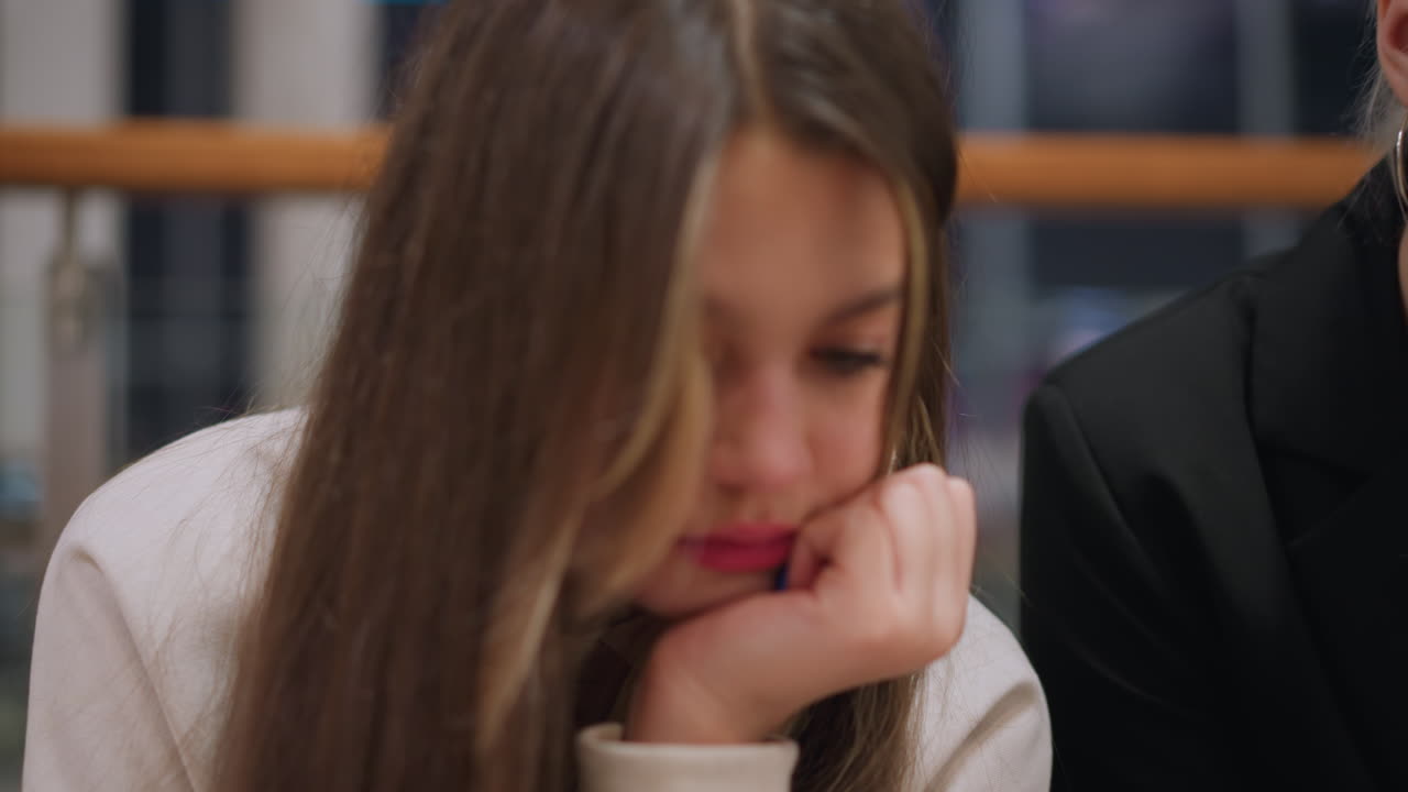 Close up of young girls sitting indoors using mobile gadgets with thoughtful focused expression reflecting youth culture digital lifestyle technology dependence modern communication