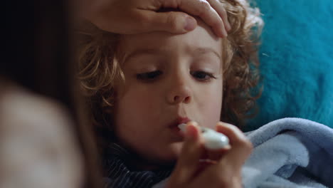 mother caring for sick child lying in bed with flu measuring temperature using thermometer little boy at home with fever mom giving health care