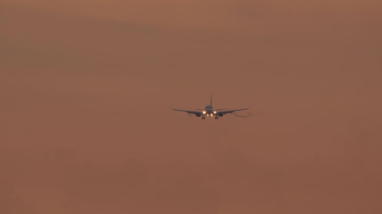 Aereo commerciale in volo con luci di atterraggio accese al tramonto.