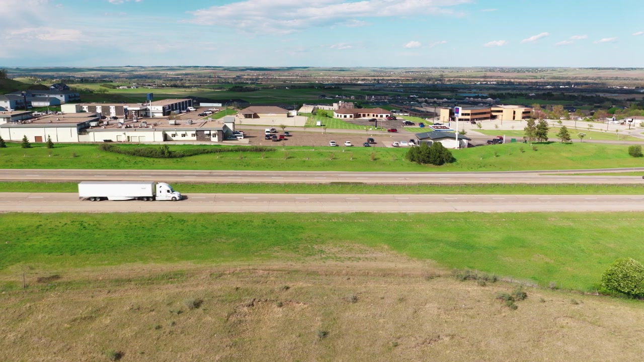Periferia commerciale di Mandan, North Dakota, che confina con l'autostrada. Attività commerciali e parcheggi di una città rurale circondati da erba verde e dolci colline