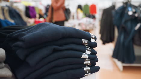 view of neatly stacked male boxer shorts with size tags (s, m, l, xl, xxl) displayed in a mall. people are seen moving in the blurred background