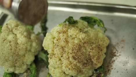 chef irreconocible rociando cabezas de coliflor con especias antes de hornear, cerrar