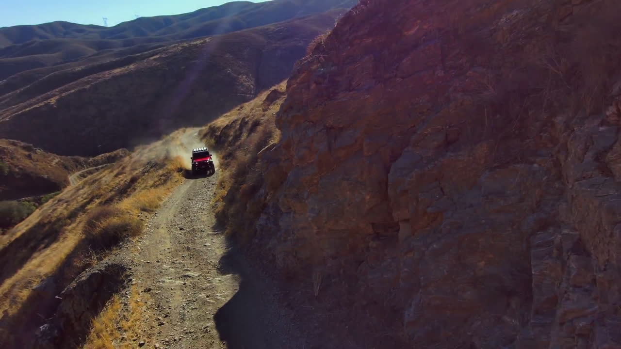jeep rojo conduciendo rápido fuera de la carretera en un sendero angosto del desierto, levantando polvo, vista aérea