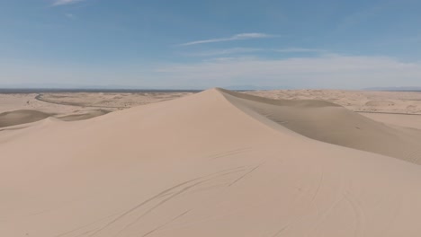 flying over sandy peak, drone shot above desert sand dune location, blue skies and soft sand