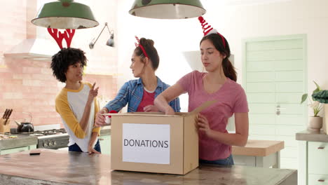 christmas time, wearing festive headbands, women friends packing donation box in kitchen for holiday