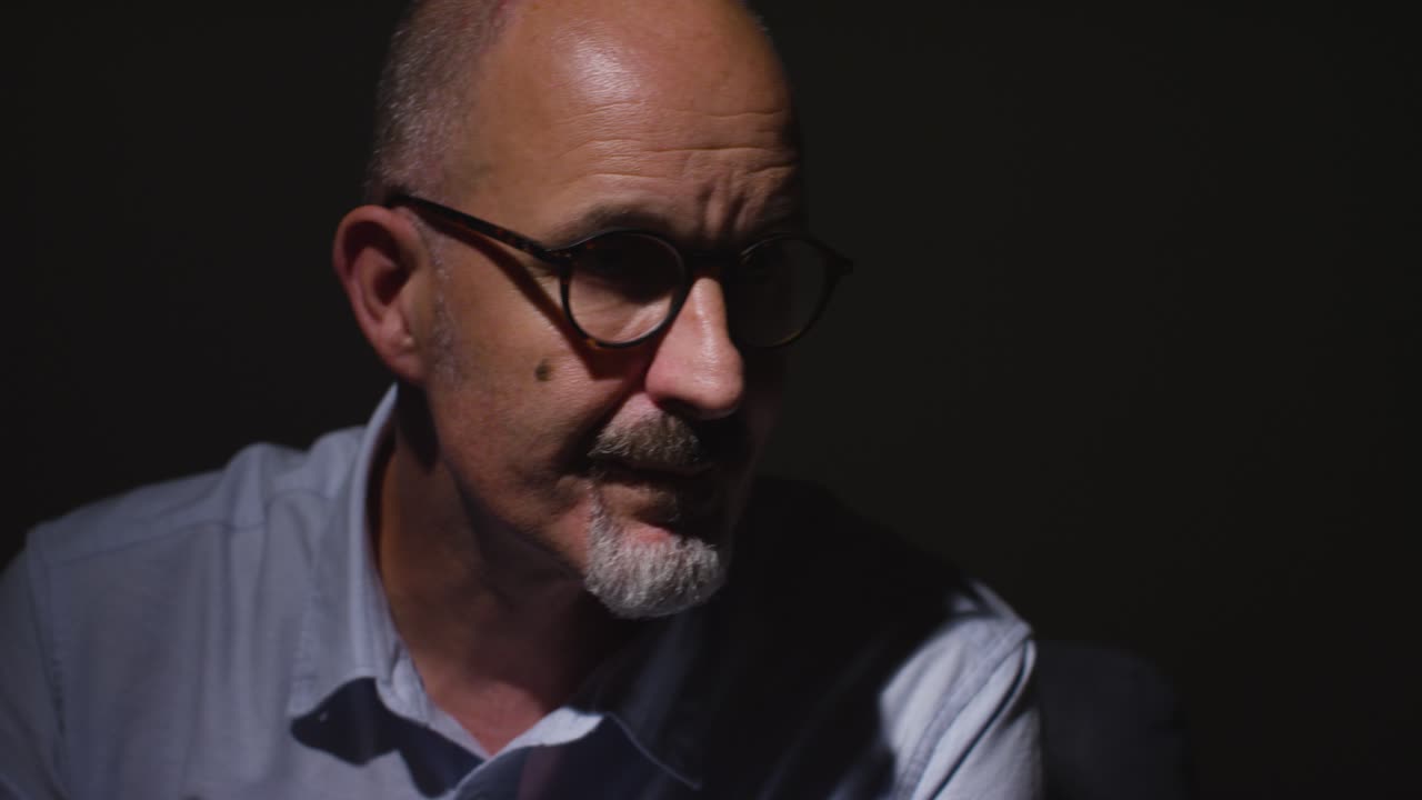 Close Up Of Depressed Mature Man Struggling With Mental Health Sitting In Darkness In Real Time With Low Key Lighting