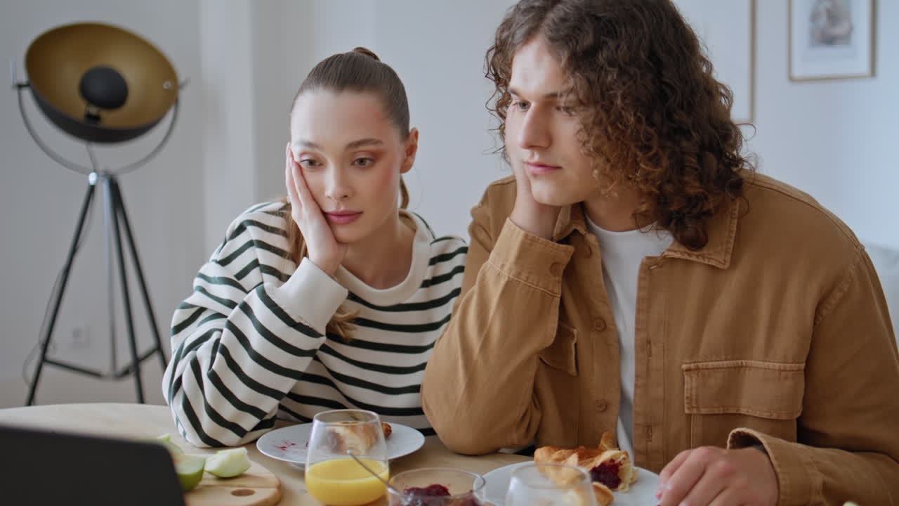 Couple worried laptop news at breakfast in kitchen closeup. Woman pointing
