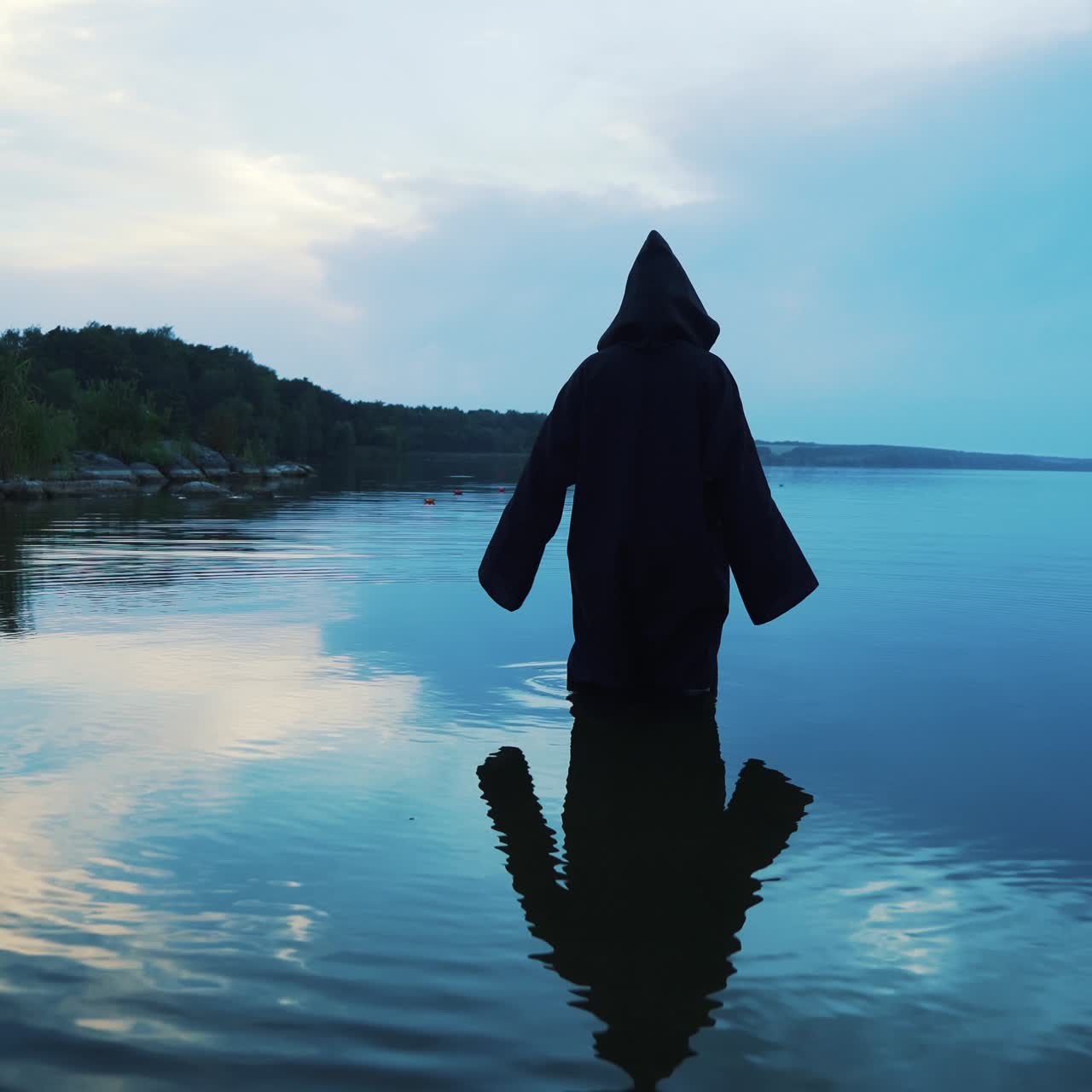 Ghost woman in the water outdoor. Scary figure in black mantle.