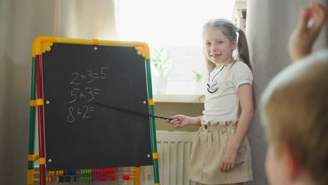 Girl-asks-little-brother-to-solve-maths-tasks-on-chalkboard