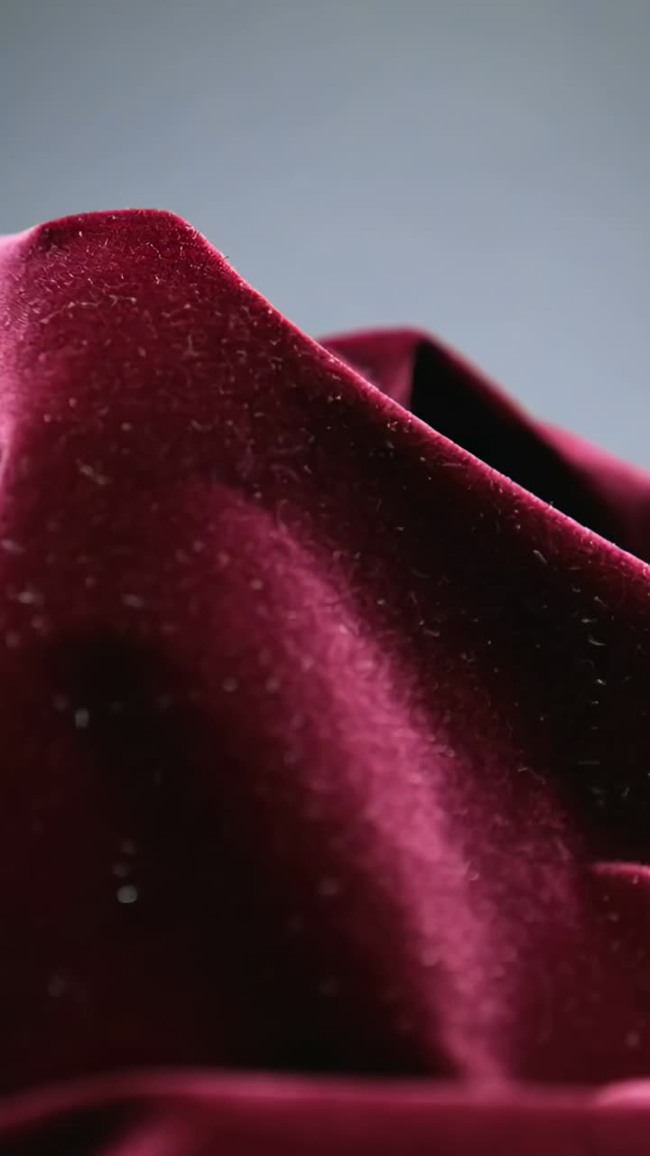 Vídeo vertical: tela de terciopelo burdeos panorámica sobre un fondo gris de estudio, que revela pelusa y textura