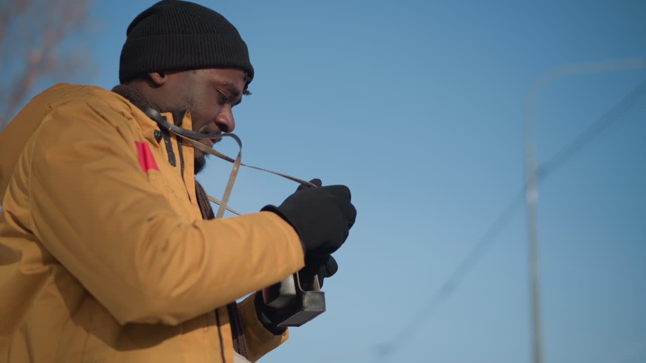 side view of reporter with camera hanging on neck holding camera out and looking around both sides while walking along snow lined city sidewalk beneath blurred tall building backdrop