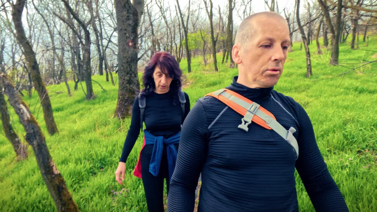 Coppia di mezza età che fa trekking insieme in un bosco fiorito primaverile. Concetto di invecchiamento sano, rimanere attivi, forma fisica e vitalità nella natura.