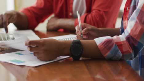 hands of biracial couple sitting at table with laptop and counting home budget