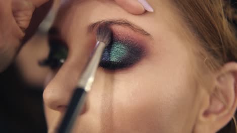 finishing eyes make up for a young woman. green colour. close view