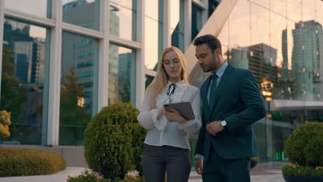 two young successful architects male and female business people outside big office building at sunset using digital tablet. collegues talking about construction project outdoor. teamwork