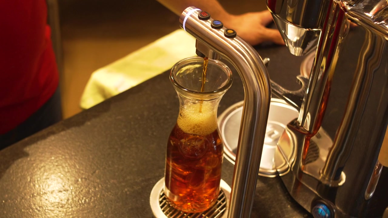 Dispenser di caffè speciale in acciaio inossidabile che riempie una caraffa di vetro con caffè freddo in un moderno bar caffetteria, attrezzatura da barista.