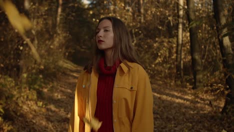 youg woman walking through autumn forrest with falling leaves