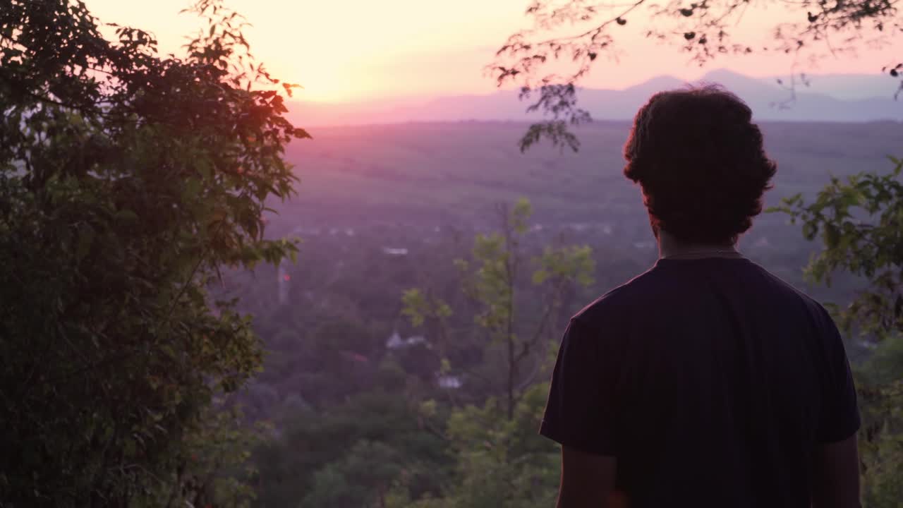 Uomo in piedi sulla cima di una collina che guarda il tramonto sulla valle