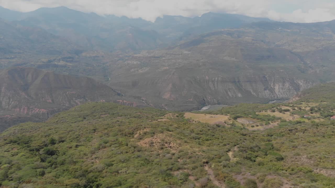 Ripresa in avanti sopra i campi con vista su montagne e fiume in un pomeriggio nuvoloso.