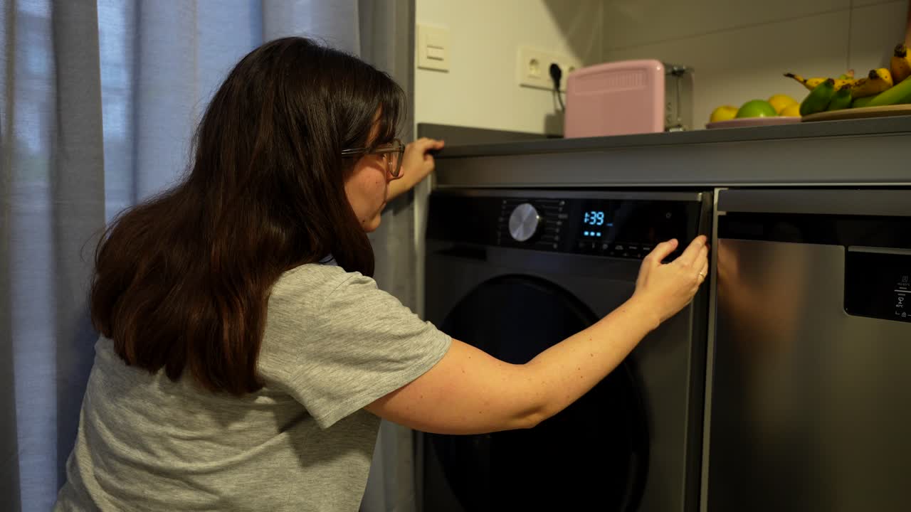 Pregnant woman bending down to put the washing machine on
