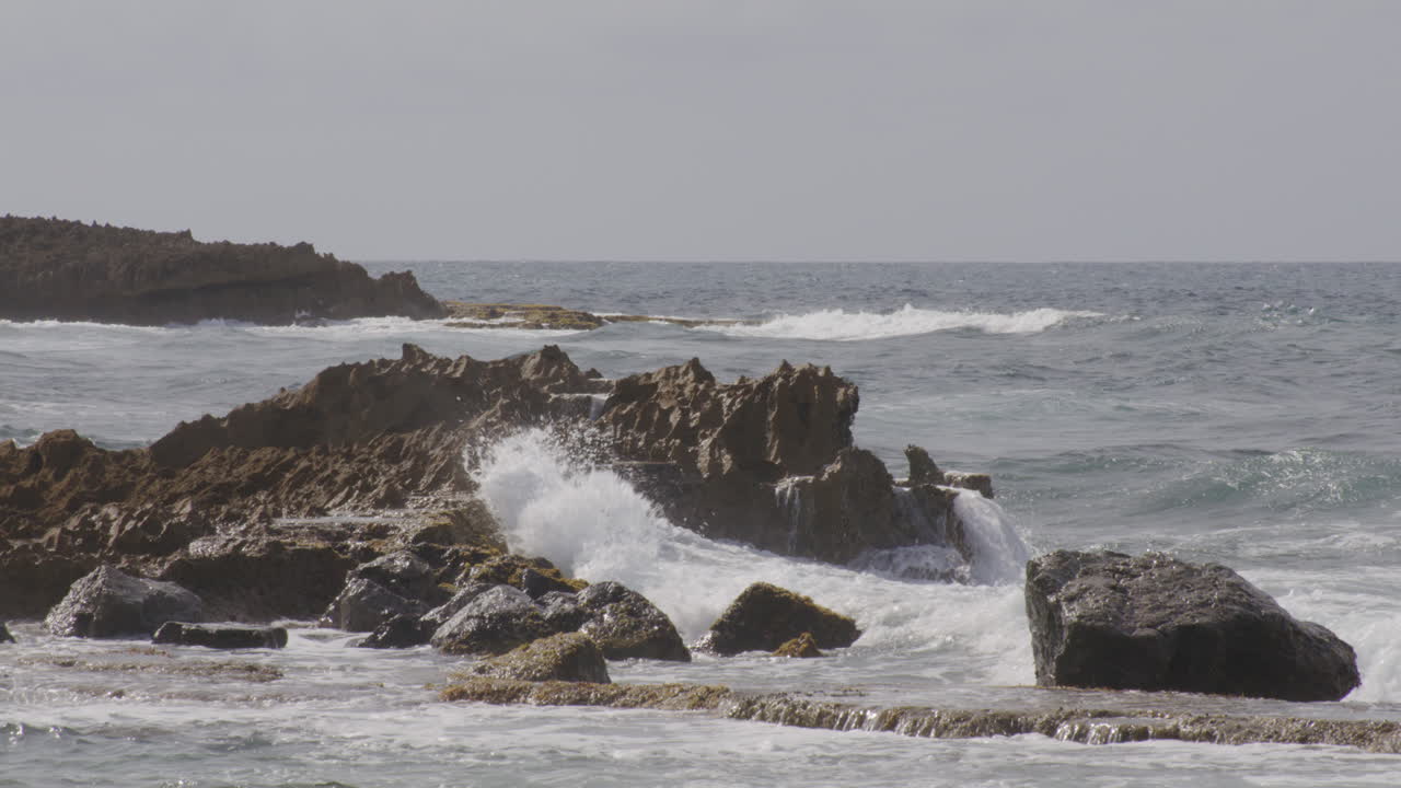 olas golpeando y salpicando en las rocas junto al mar de la playa en un día nublado