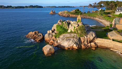 drone moves back from sentinelle oratory, revealing nearby houses, rocky shore, sea, and port-blanc bay.