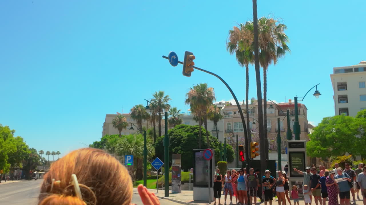 Busy street scene in Málaga, Spain, with palm trees, tourists, and a cyclist crossing at a pedestrian zone on a sunny day, highlighting the lively urban atmosphere