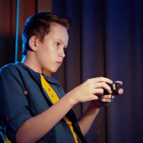 side view of a boy playing games at home. serious teenager plays video game using joystick and becomes happy when he wins.