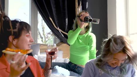 hipster blonde girl sitting on the bed and recording a video of her friends who drinking wine and eating pizza at home